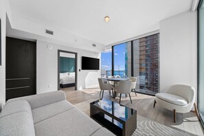A modern living room with a sofa, a coffee table, and a dining area with chairs. There is a large window providing a view of the cityscape. - 30th Floor Luxury Suite with Bay Views & Rooftop Pool (Miami)