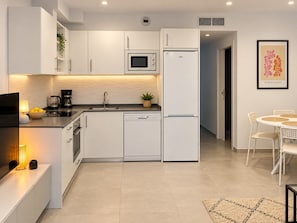 Eine moderne Küche mit weißen Schränken, einer Mikrowelle, einem Kühlschrank und einem Essbereich mit Tisch und Stühlen.