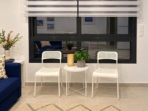 Ein Zimmer mit einem blauen Sofa, zwei weißen Stühlen, einem kleinen runden Tisch und einer Topfpflanze.