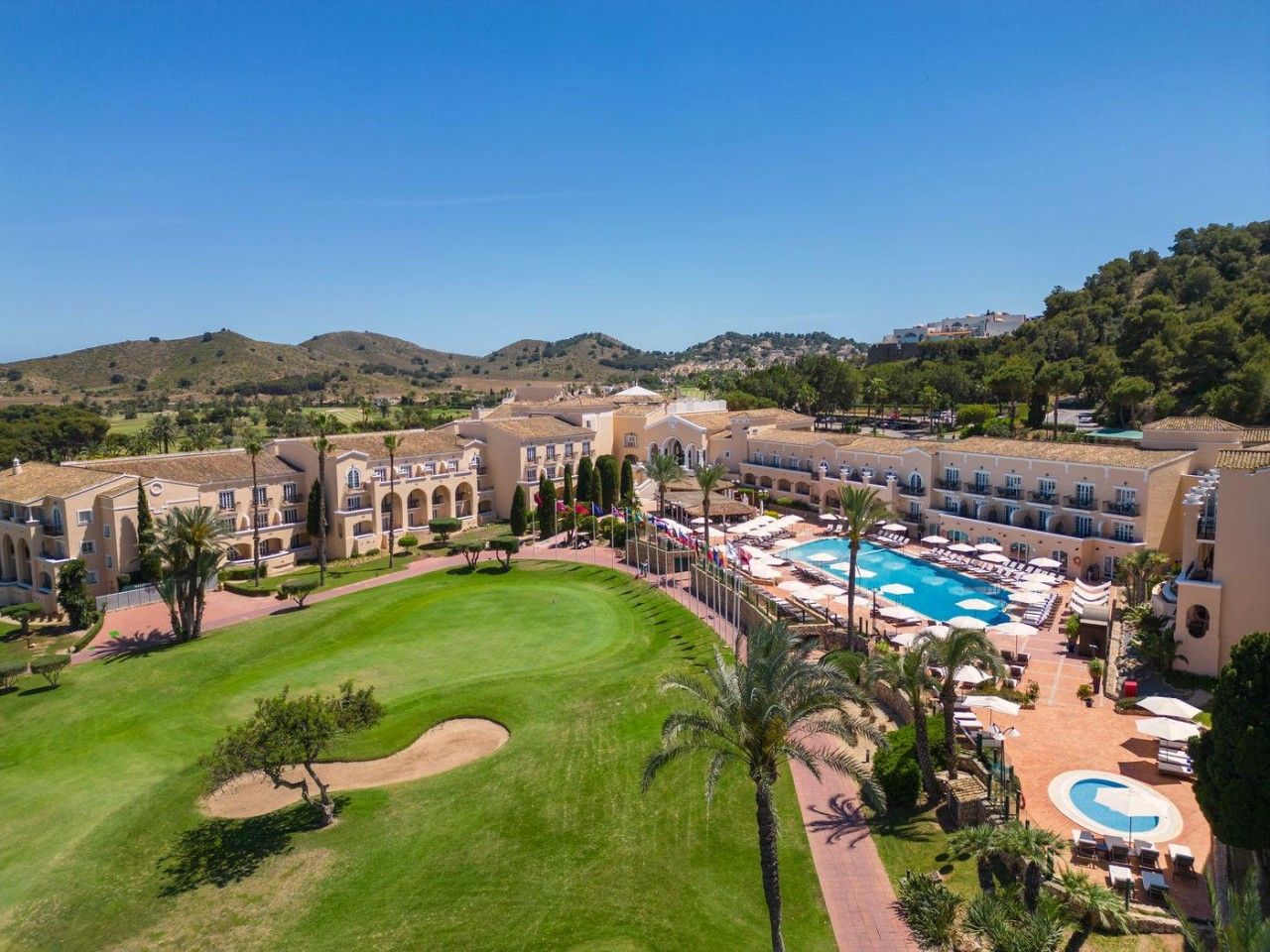 Een resort met een groot zwembad, verschillende gastenkamers en een verzorgd gazon.