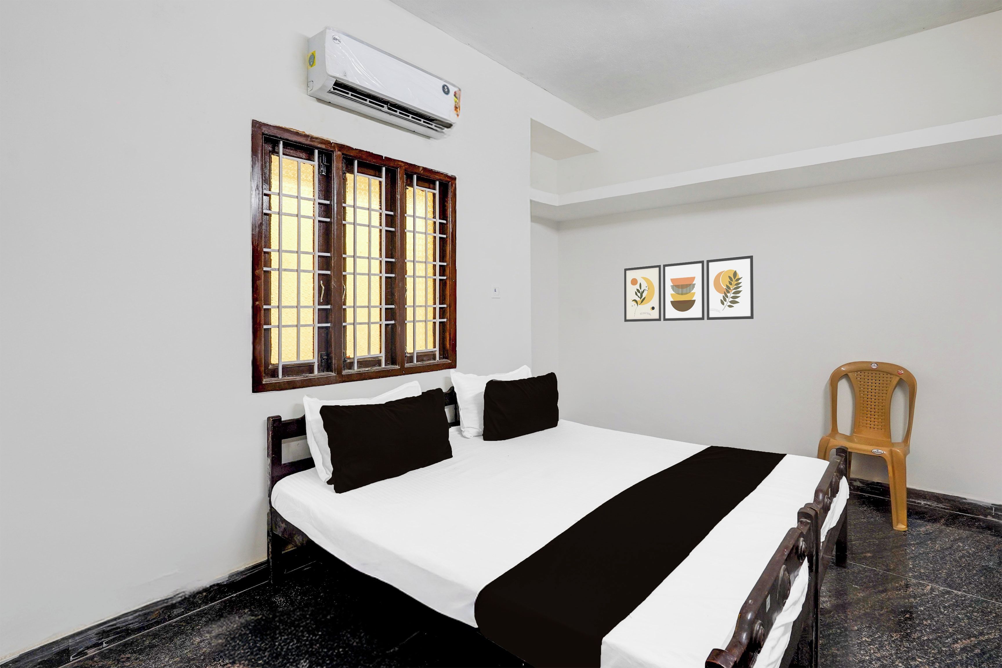 A hotel room with a bed, a window with bars, an air conditioner, and a chair.