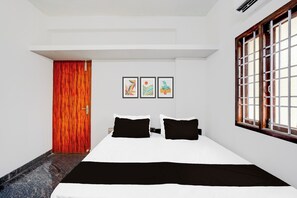 A bedroom with a bed, a window with bars, a door, and three framed pictures on the wall.