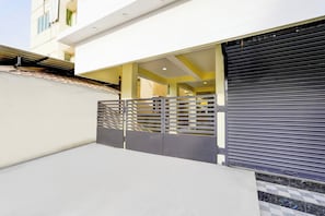 A modern building entrance with a gated driveway and a closed roller shutter.