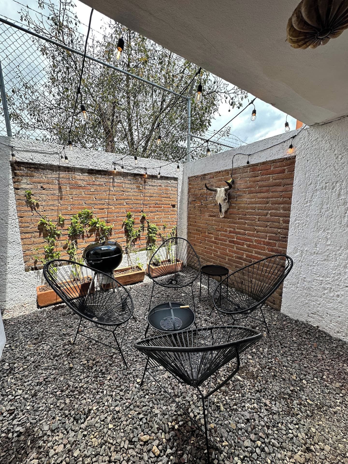 An outdoor patio with a brick wall, a grill, and metal chairs.