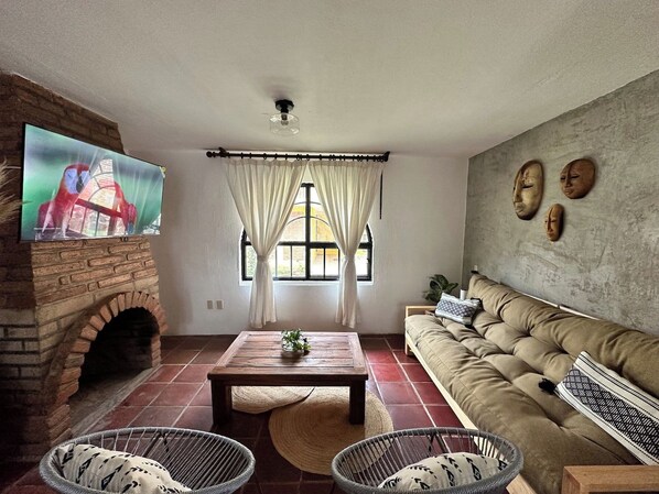 A living room with a brick fireplace, a television, a sofa, and a window with curtains.