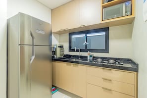 A compact kitchen with a stainless steel refrigerator, a microwave, a gas stove, and beige cabinets. - Cais Eco #106 - Beachfront Resort by Carpediem (Ipojuca)