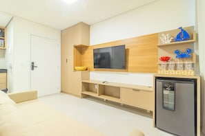 A modern living room with a flat-screen TV mounted on a wooden wall, a built-in kitchen area with a refrigerator, and a seating area with a sofa. - Cais Eco #106 - Beachfront Resort by Carpediem (Ipojuca)