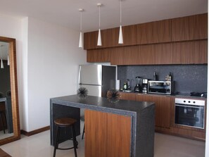 Uma cozinha moderna com armários de madeira, uma ilha central com banquetas, geladeira, micro-ondas, cafeteira e forno.