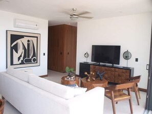 Een moderne woonkamer met een witte bank, een televisie, een houten kast en een plafondventilator.