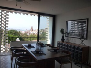 Uma área de refeições com vista para a paisagem urbana, um ventilador de teto e uma mesa de jantar moderna com cadeiras.