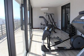 Ginásio com equipamentos de exercício, janelas amplas e uma varanda com vista.
