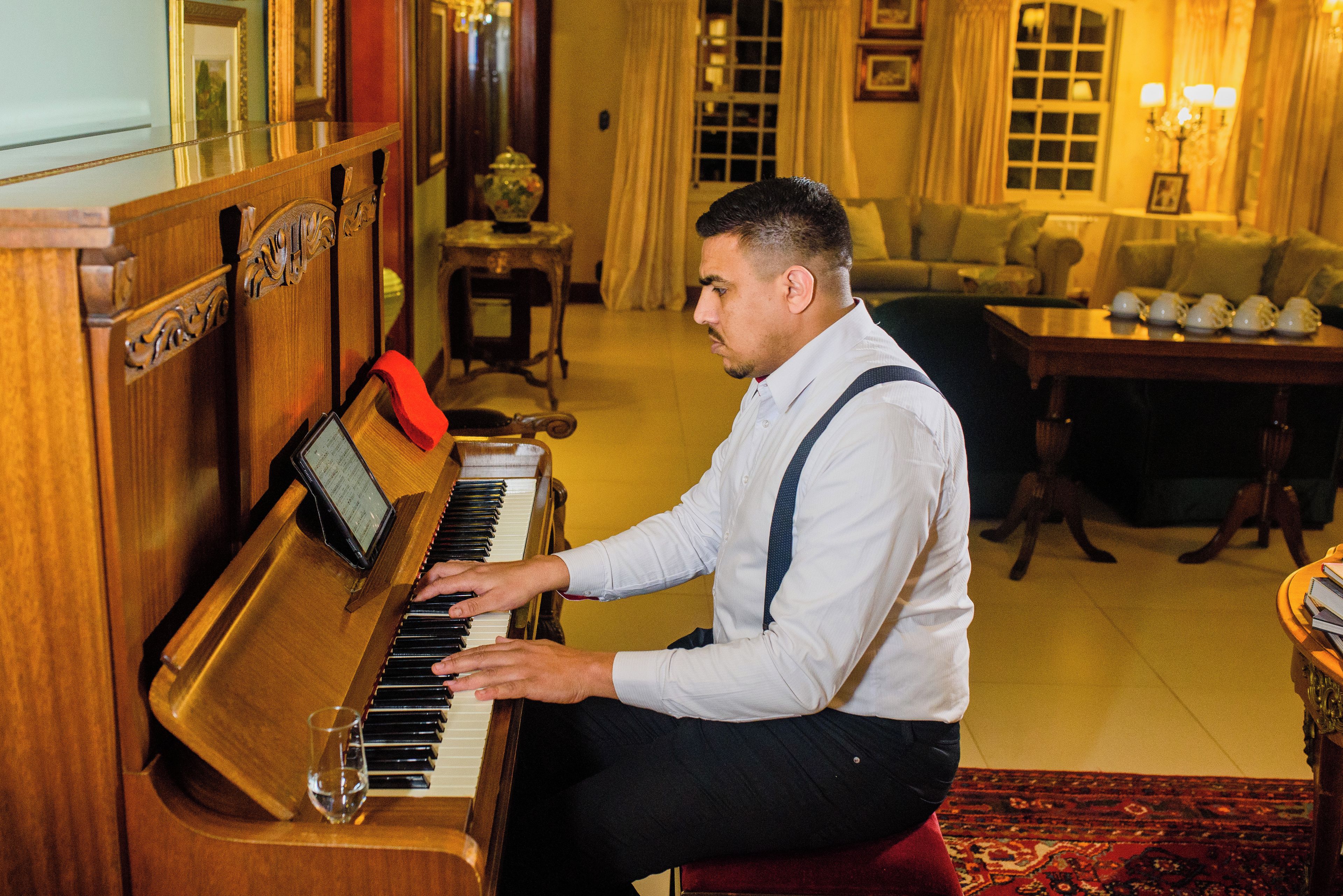 Une personne joue du piano à queue dans une pièce où se trouvent un canapé, une table avec des tasses à thé et un tapis à motifs.