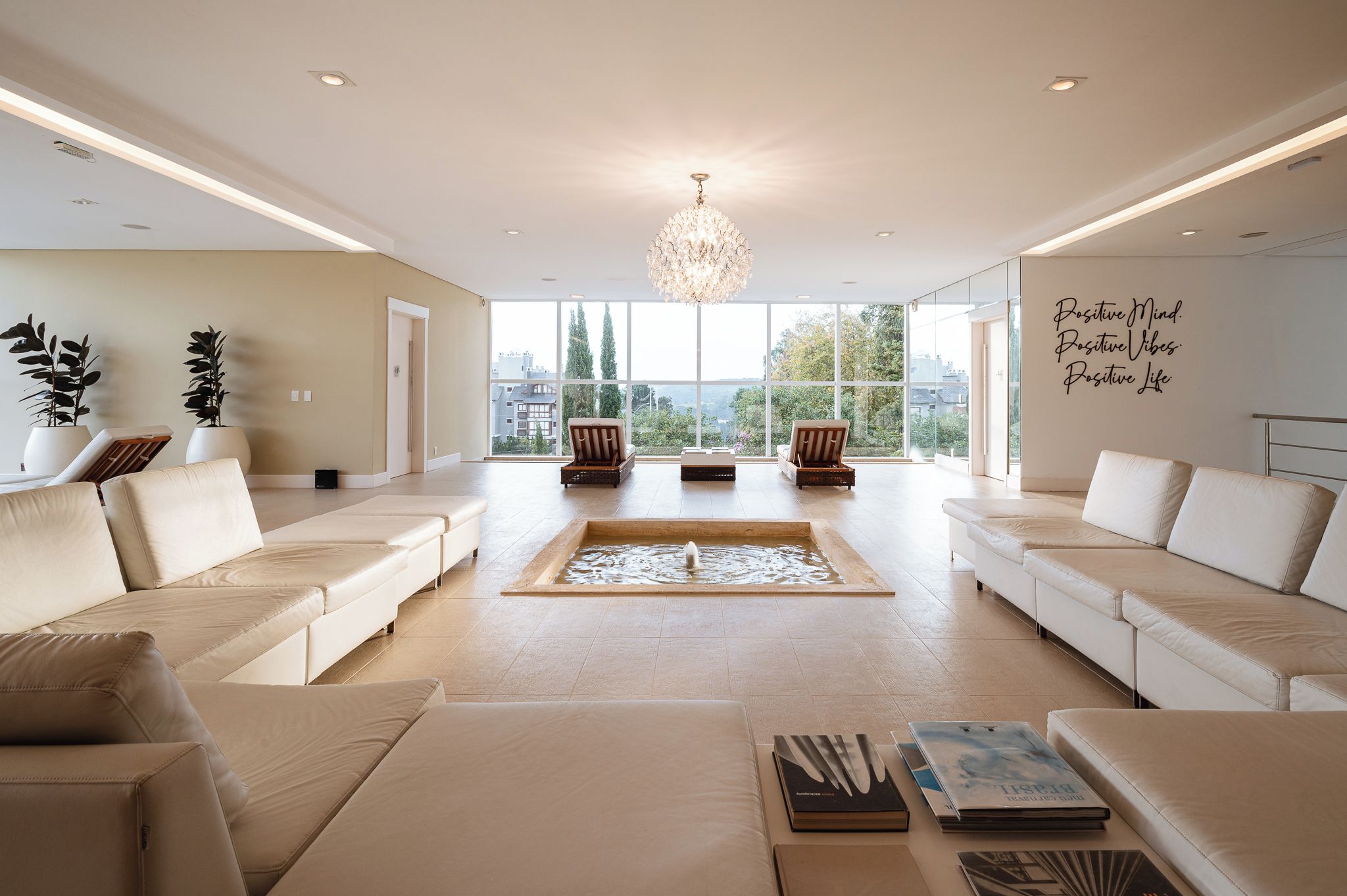 A spacious living room with a large window, a chandelier, and a motivational quote on the wall.