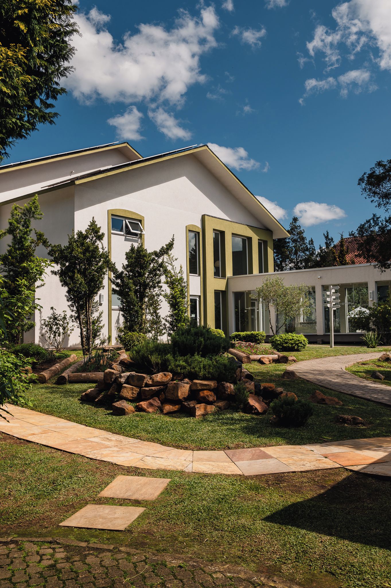 A modern building with a flat roof, large windows, and a well-maintained garden with a stone pathway.
