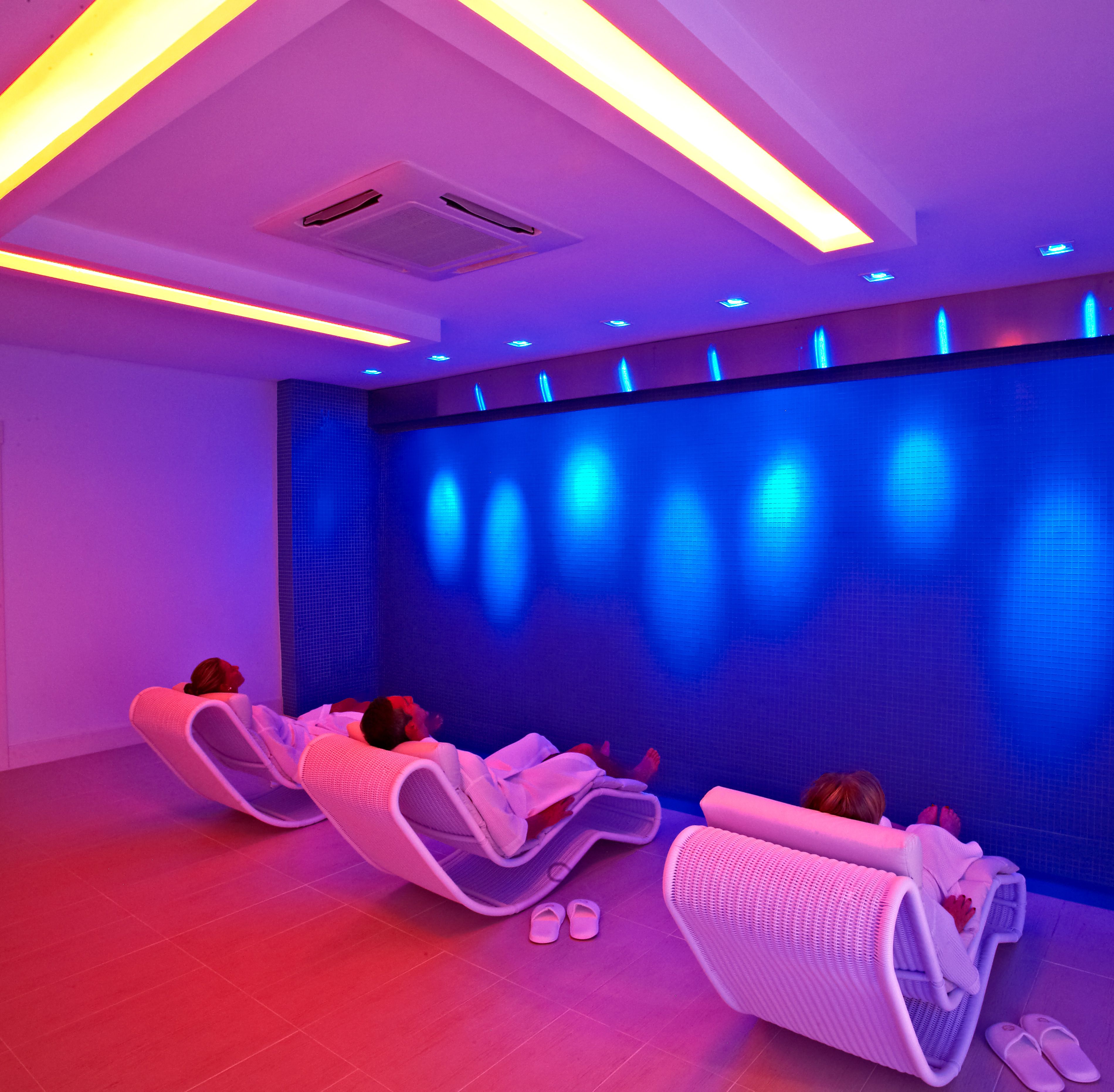 Una habitación con sillones de masaje e iluminación azul en una gran pared.
