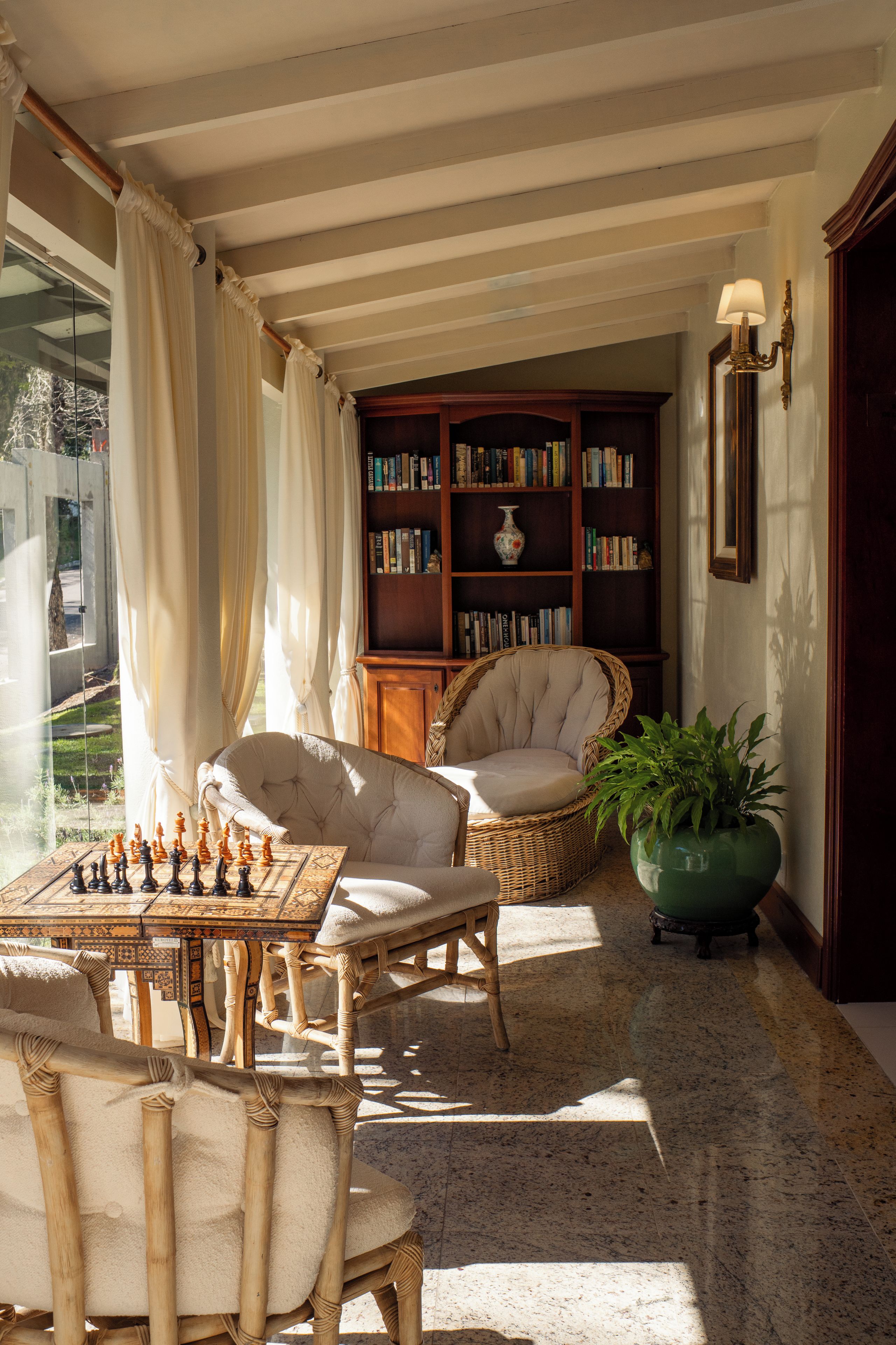 A room with a chessboard, two chairs, a bookshelf, and a potted plant.