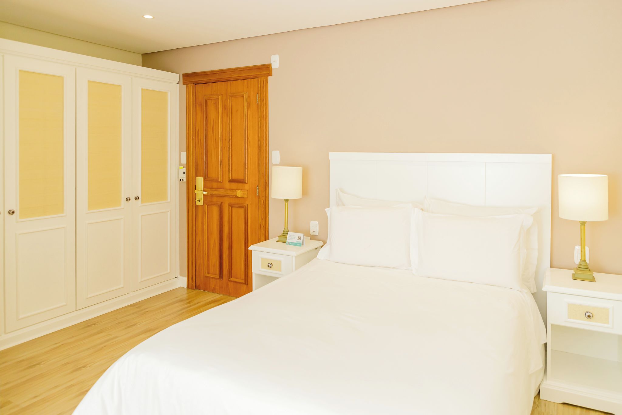 Habitación de hotel con una cama grande, dos mesitas de noche con lámparas, un armario de madera y una puerta.