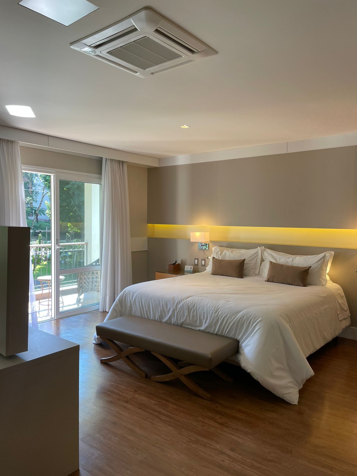 Une chambre d’hôtel avec un grand lit, une banquette, un bureau et une vue à travers la porte vitrée.