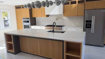 A modern kitchen with wooden cabinets, a marble countertop, a stainless steel refrigerator, and a gas stove.