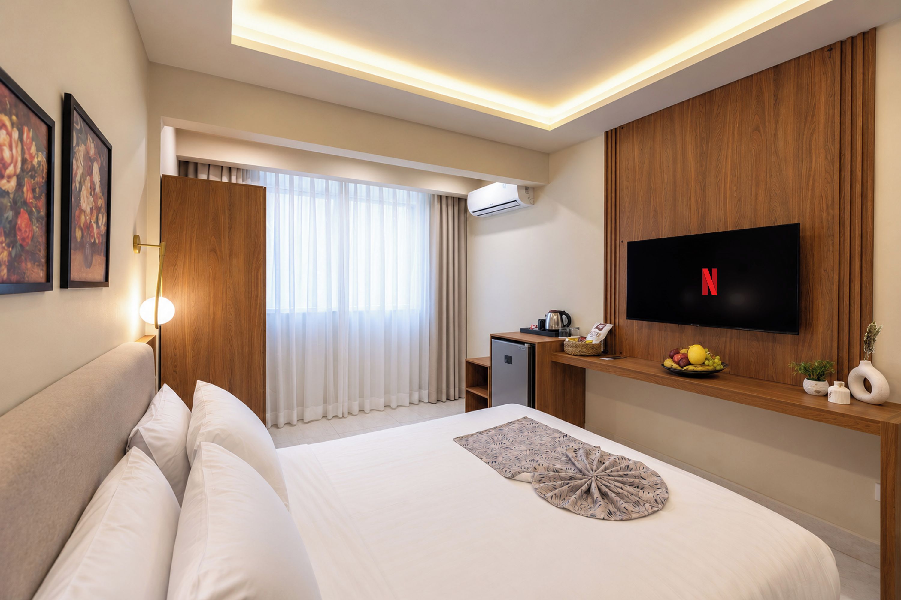 Habitación de hotel con cama, televisor de pantalla plana en la pared, kitchenette pequeña y ventana con cortinas.