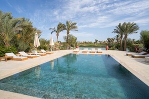 A clear swimming pool with lounge chairs and umbrellas, surrounded by palm trees and a view of distant buildings. - Lagoon Front Villa Private Pool El Gouna (El Gouna)