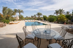 A poolside area with a glass table and chairs, lounge chairs, and palm trees. - Lagoon Front Villa Private Pool El Gouna (El Gouna)