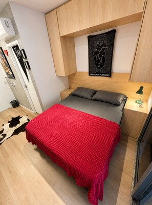 Ein gemütliches Schlafzimmer mit Bett, Kopfstütze, Wandkunst, Nachttisch mit Lampe und einem kleinen Teppich.
