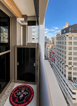 Ein Balkon mit Glastür, einem kleinen Teppich und Blick auf die Stadtlandschaft.