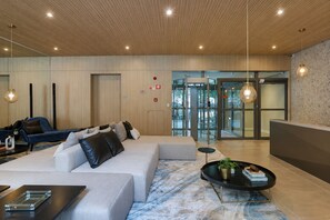 Eine moderne Hotelhalle mit einer Sitzecke, einem Empfangsbereich und einem Eingang zu einem gläsernen Aufzug.