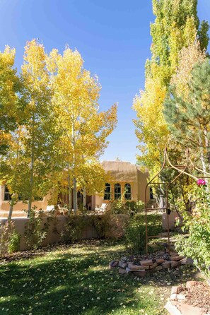 A courtyard with trees, a building with arched windows, and a brick fire pit. - Taos luxury upscale private secluded gourmet kitchen mountain views upgrade (Arroyo Seco)