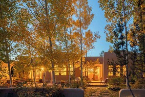 A courtyard with trees, outdoor seating, and a building with large windows. - Taos luxury upscale private secluded gourmet kitchen mountain views upgrade (Arroyo Seco)