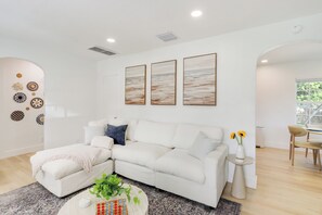 Un salon moderne avec un canapé d’angle blanc, une table basse agrémentée d’une plante et des œuvres d’art accroch ées au mur.