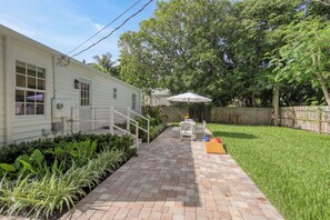 Un jardin avec une terrasse, une maison blanche et une clôture en bois.