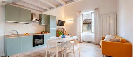 A modern kitchen with a dining area, a sofa, and a view of a building outside.