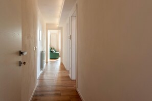 A hallway with wooden flooring leading to a room with a green sofa. - Duomo 10 min · 2 separate bedrooms · Lift (FIRENZE)