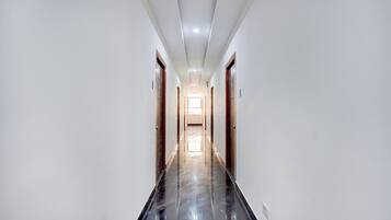 A long, narrow hallway with white walls and a shiny black floor, leading to a bright room at the end.