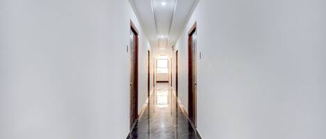 A long, narrow hallway with white walls and a shiny black floor, leading to a bright room at the end.