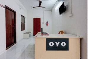 A reception desk with a sign reading 'OYO' in a hallway with a ceiling fan, a fire extinguisher, and a television mounted on the wall.