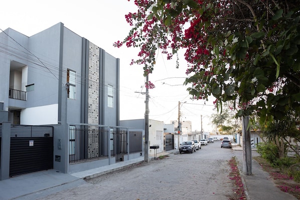 A narrow urban street with modern buildings, a gated entrance, and parked cars. - Residencial Laris - Lofts in Feira de Santana by Carpediem (Feira de Santana)