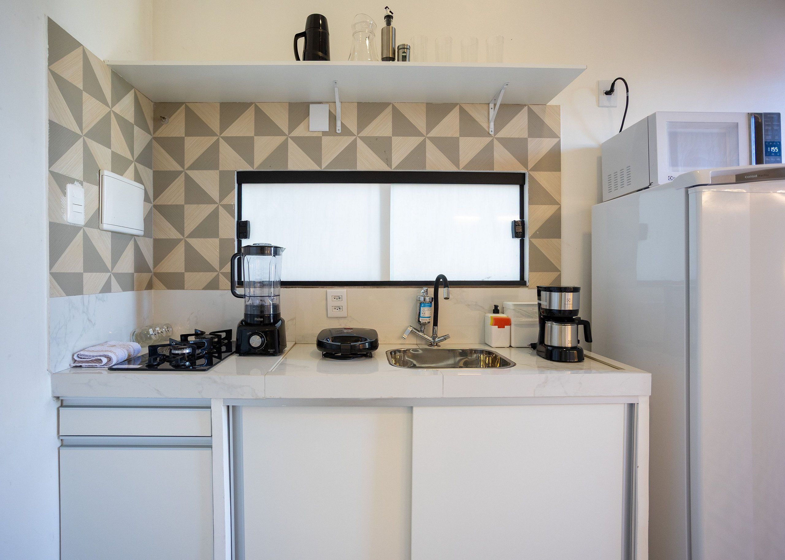 A compact kitchen with a microwave, coffee maker, blender, and a sink.