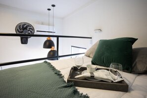 A neatly made bed with a tray of glasses and a napkin, a green pillow, and a dark green throw blanket.