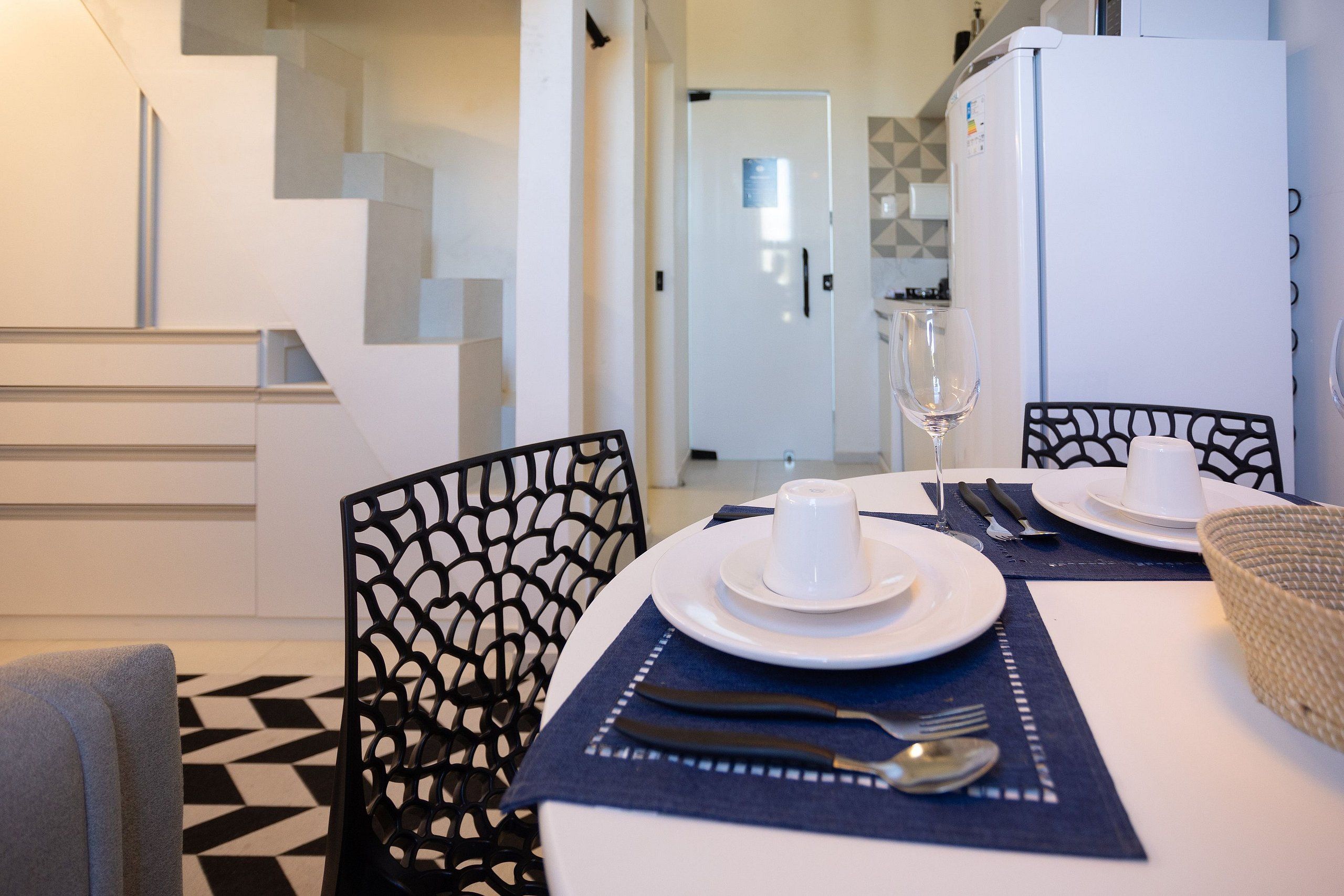 A dining area with a table set for two, featuring white plates, a glass, cutlery, and a woven basket.