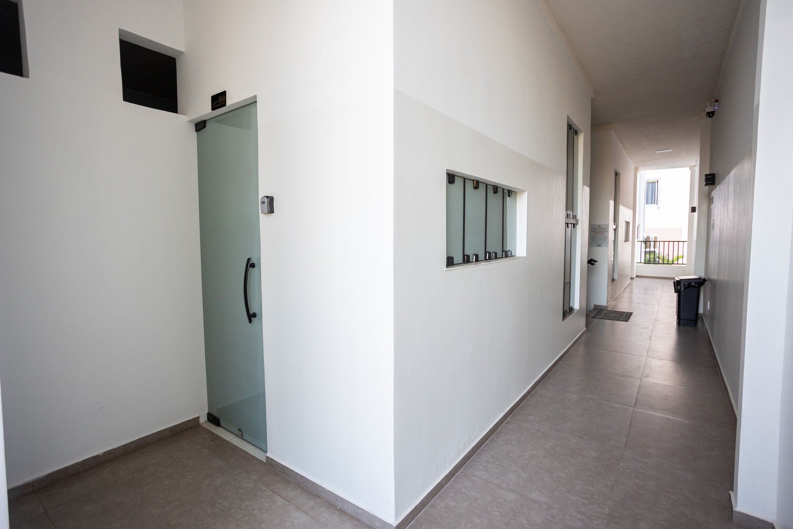 A corridor with a glass door, a wall-mounted security camera, and a trash bin.