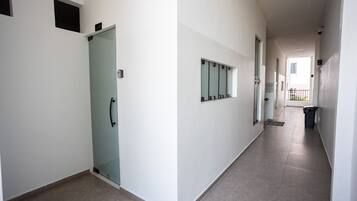 A corridor with a glass door, a wall-mounted security camera, and a trash bin.