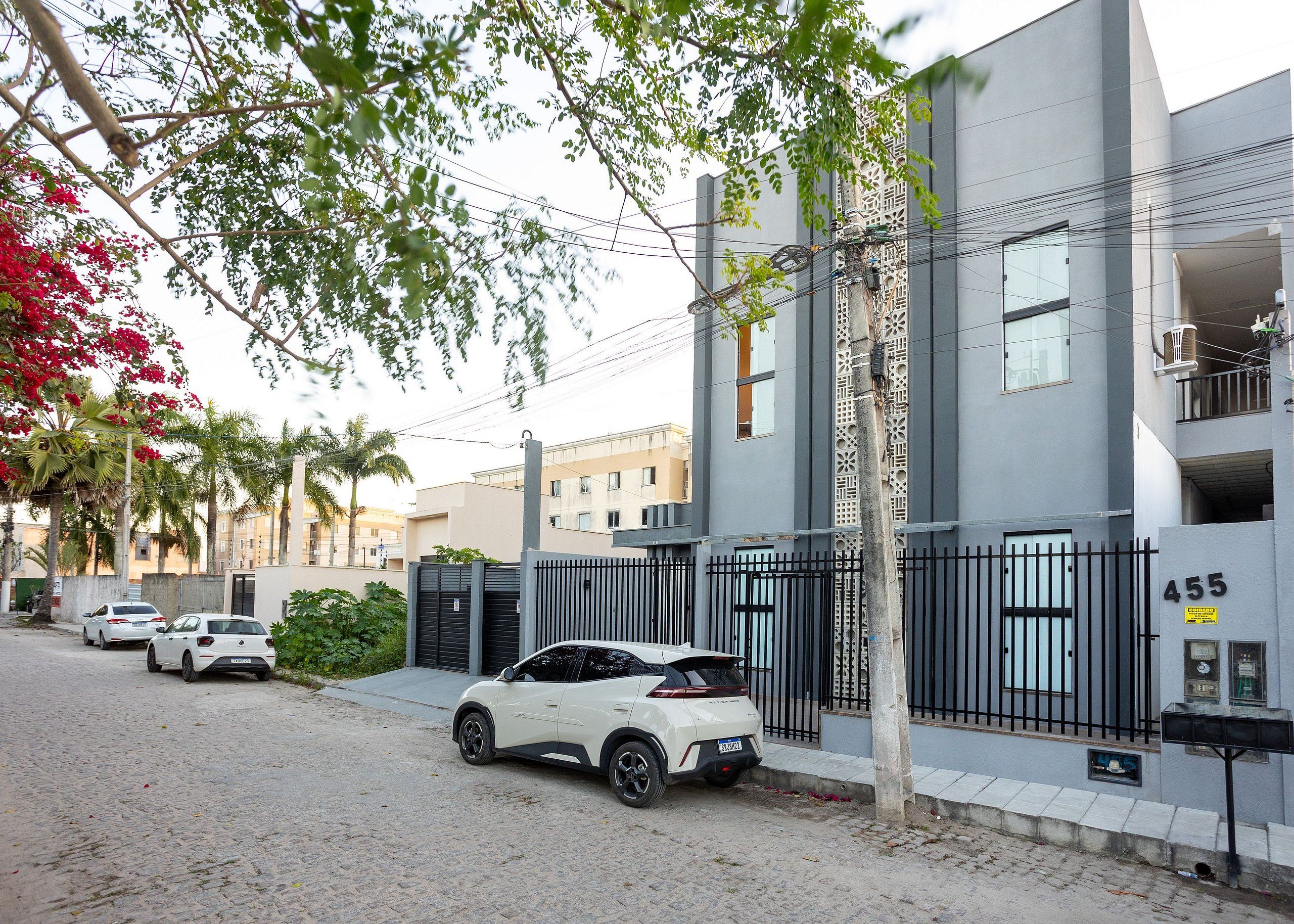 Un edificio moderno con entrada protegida por un portón, buzón y calle con automóviles estacionados.