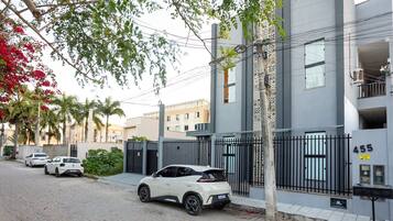 Un edificio moderno con entrada protegida por un portón, buzón y calle con automóviles estacionados.
