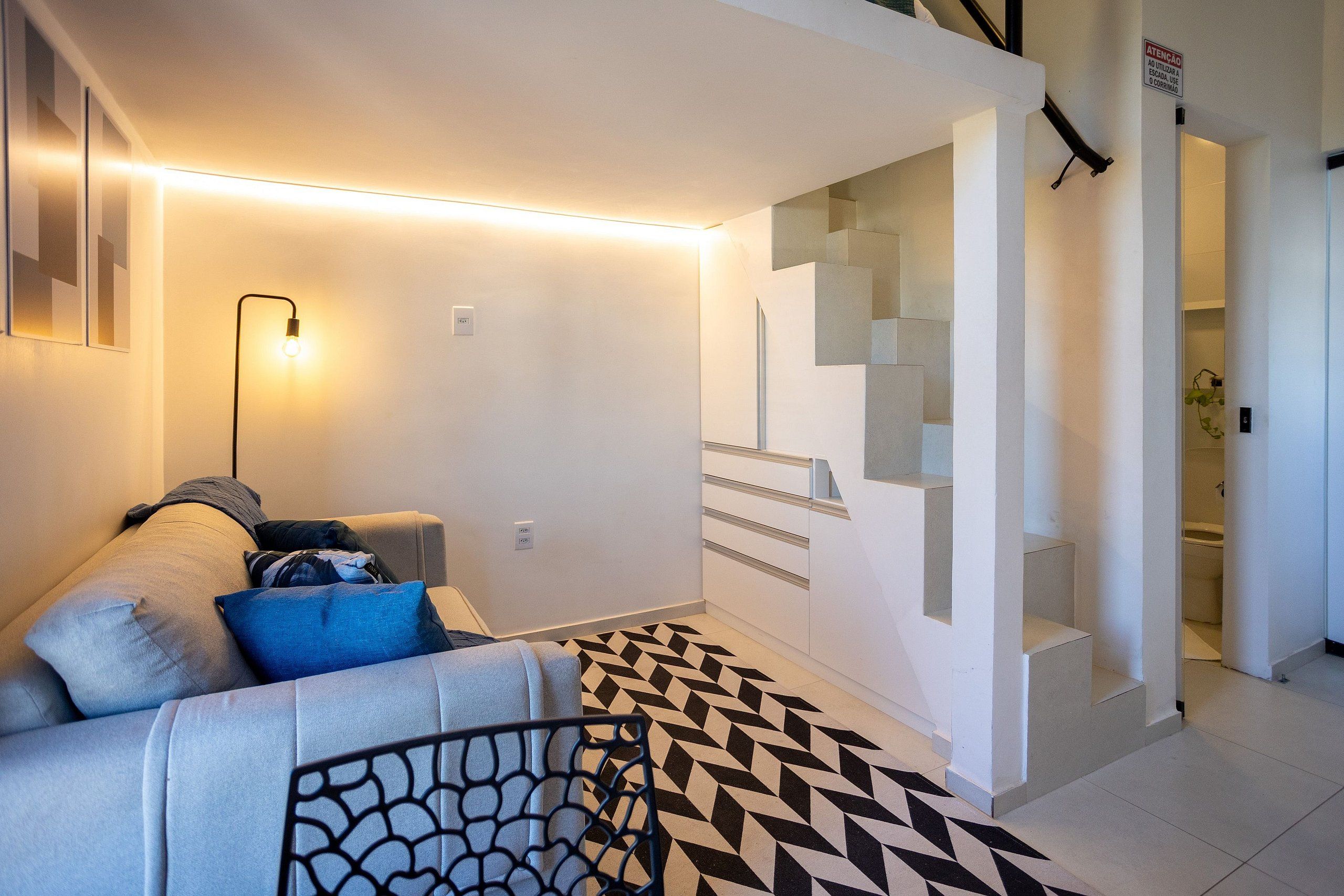 Uma sala de estar moderna com um sofá, um tapete estampado e uma escada que leva a um andar superior.