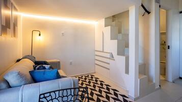 Uma sala de estar moderna com um sofá, um tapete estampado e uma escada que leva a um andar superior.