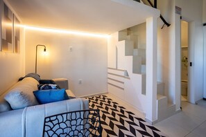 A modern living room with a sofa, a patterned rug, and a staircase leading to an upper level.