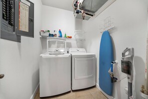 A laundry room with two washing machines, a dryer, and a blue ironing board. - Land's End Condo - Ideal location & great view! (Osage Beach)